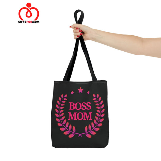 A person carrying a black tote bag that proudly boasts Boss Mom in pink lettering, embraced by a laurel wreath and stars.
