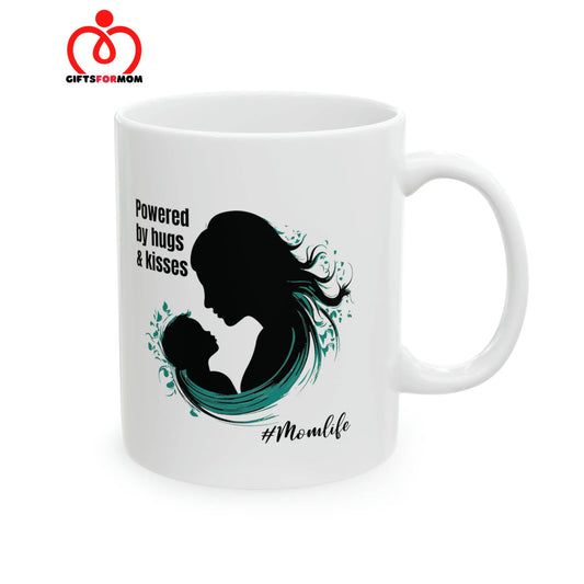 A white coffee cup from the Gifts For Mom store, featuring a silhouette of a woman and child alongside the text Powered by hugs & kisses. The hashtag #Momlife is below the image.