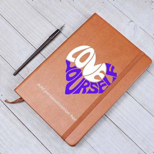 A vegan leather journal featuring an engraved heart made up of the word "love" in white and "yourself" in purple. This journal from the Gifts For Mom store is personalizable.