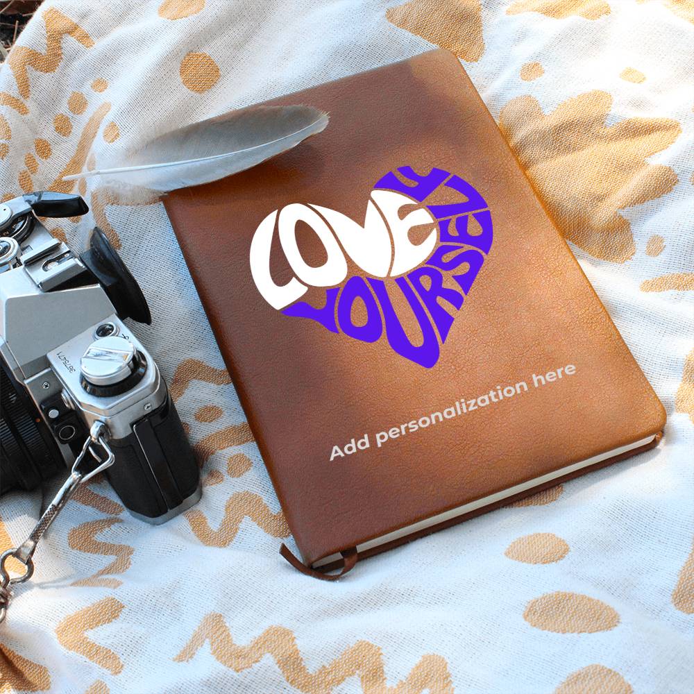A vegan leather journal featuring an engraved heart made up of the word "love" in white and "yourself" in purple. This journal from the Gifts For Mom store is personalizable.