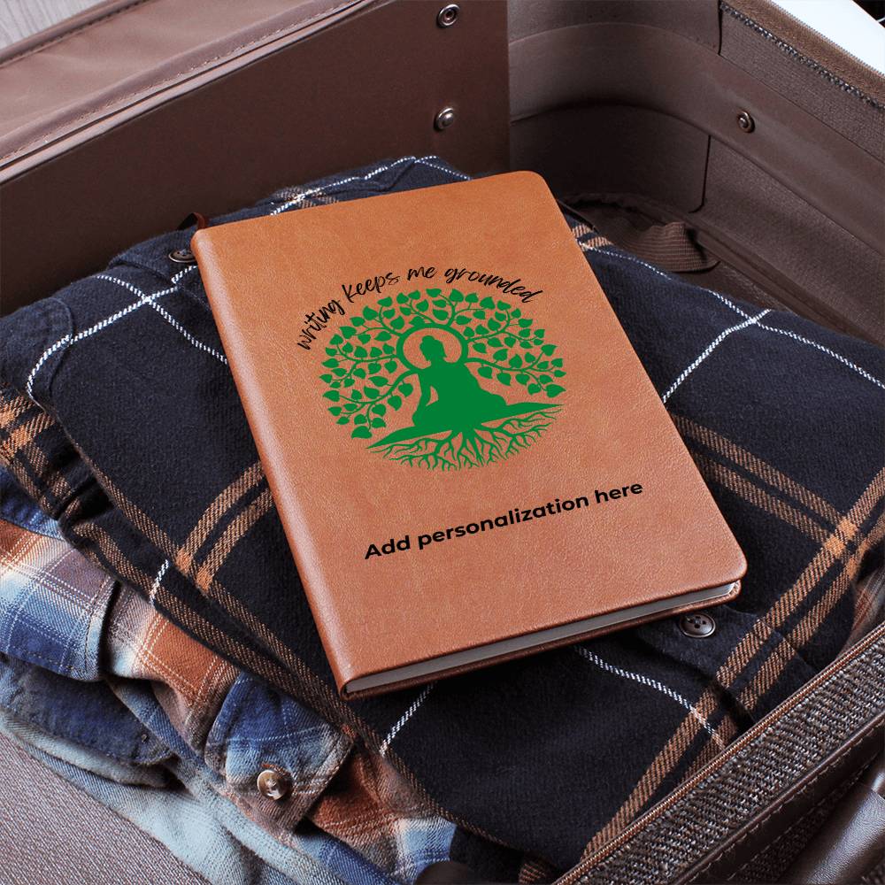 A vegan leather journal featuring an engraved green tree, roots, and a person design beautifully displays the phrase writing keeps me grounded. This journal from the Gifts For Mom store is personalizable.
