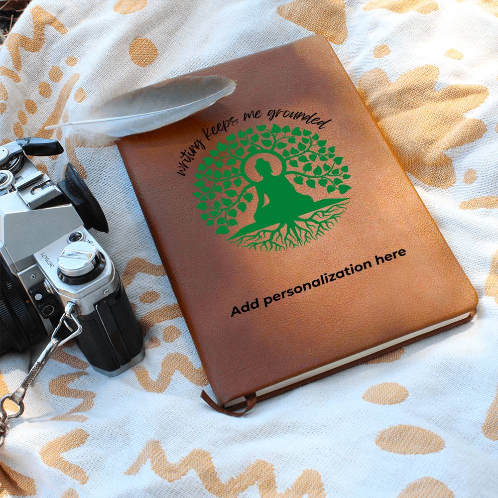A vegan leather journal featuring an engraved green tree, roots, and a person design beautifully displays the phrase writing keeps me grounded. This journal from the Gifts For Mom store is personalizable.