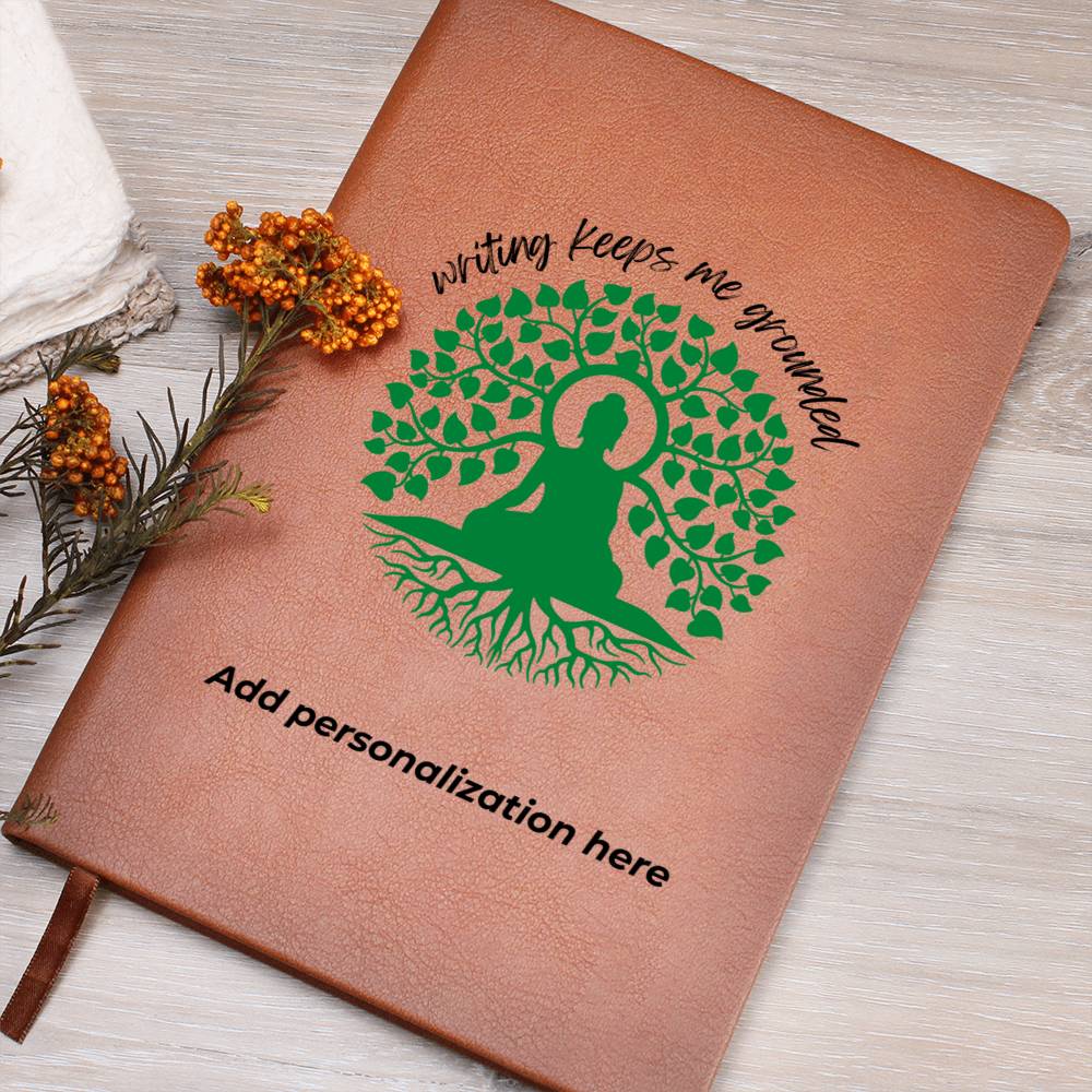 A vegan leather journal featuring an engraved green tree, roots, and a person design beautifully displays the phrase writing keeps me grounded. This journal from the Gifts For Mom store is personalizable.